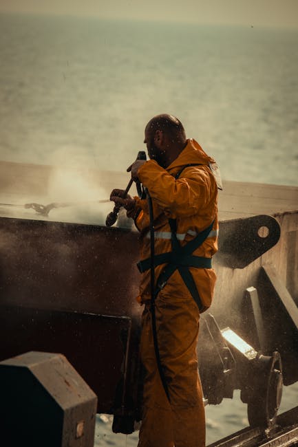 Sarı yağmurluk giymiş bir işçi, okyanus manzarası eşliğinde bir gemi güvertesinde ekipmanı çalıştırıyor.