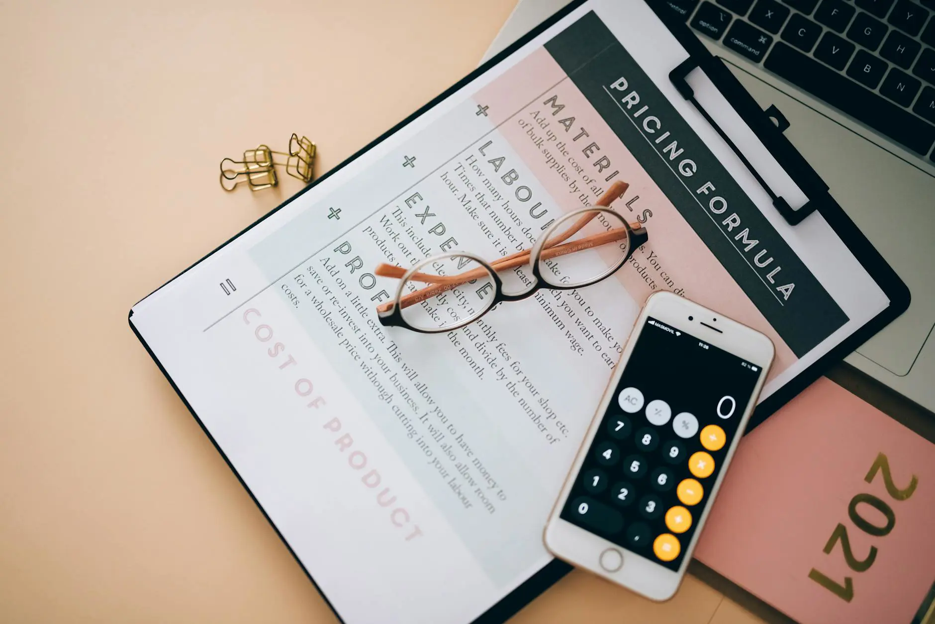 Overhead view of business tools including calculator, pricing documents, and eyeglasses on a desk