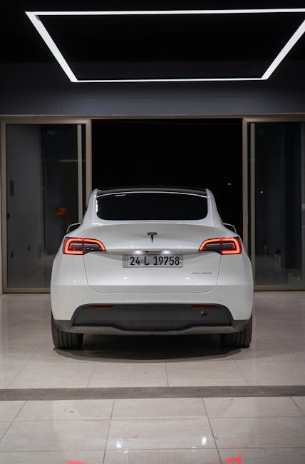 Minimalist bir kapalı showroom ortamında beyaz bir Tesla Model Y'nin arka görünümü.