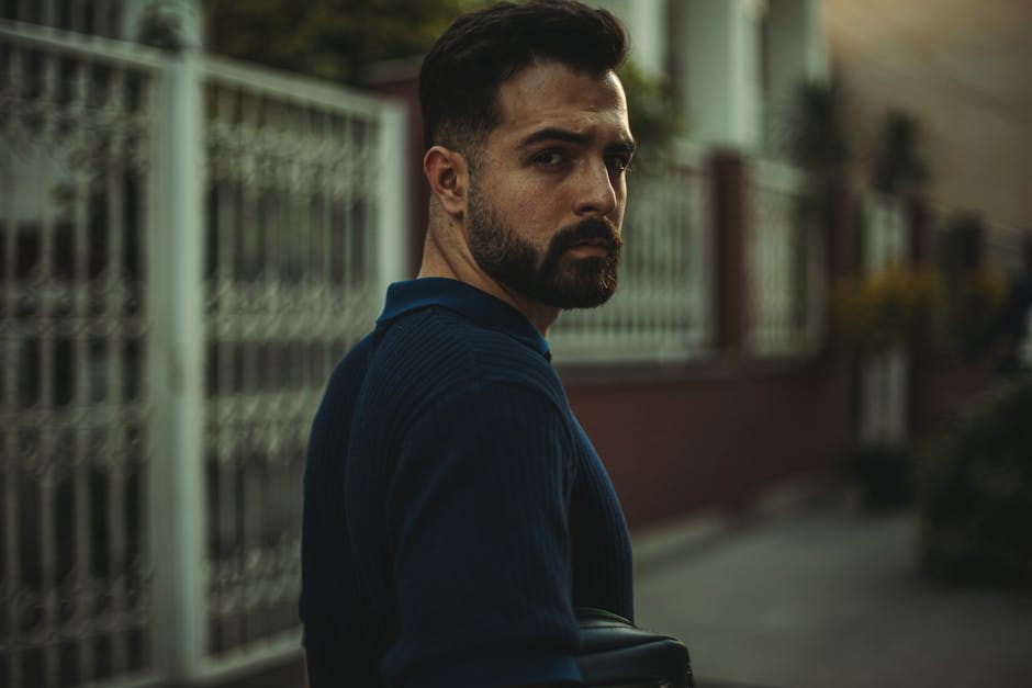 Dışarıda yürüyen mavi kazaklı adam, kameraya bakıyor, kasvetli akşam ışığı.