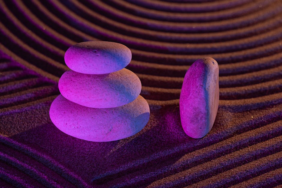 Mor ışık altında üst üste dizilmiş taşlardan oluşan, kum desenleriyle çevrili, denge ve huzuru simgeleyen sakin bir Zen bahçesi.