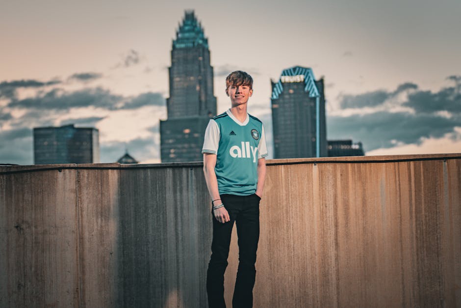 Gün batımında şehrin silüetinin önünde spor forması giymiş genç bir yetişkin poz veriyor.