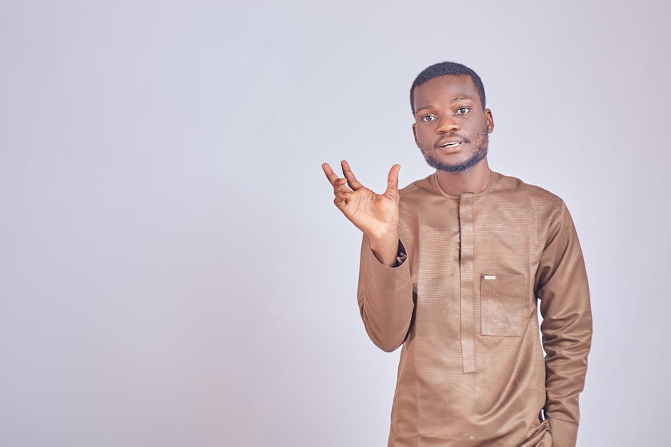 Geleneksel kıyafetler içinde, nötr bir arka plan önünde, ifadeli hareketler yapan kendine güvenen bir adamın portresi.