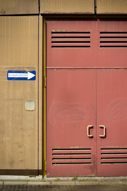 Kırmızı endüstriyel kapı ve Einbahnstraße tabelası, kentsel sokak mimarisini simgeliyor.