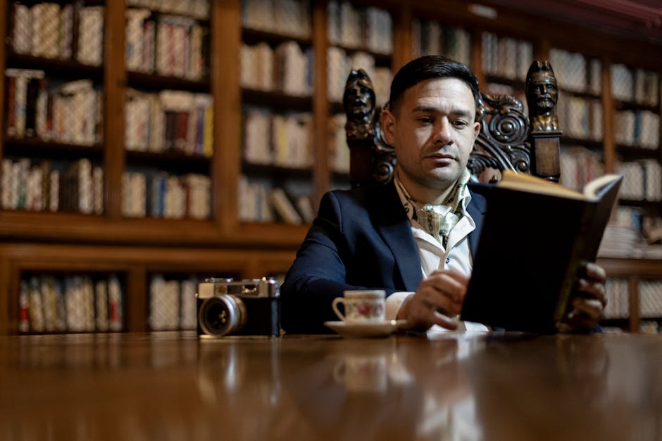 Bir adam, sofistike bir kütüphanede kitap okuyor, zarafet ve incelik saçıyor.