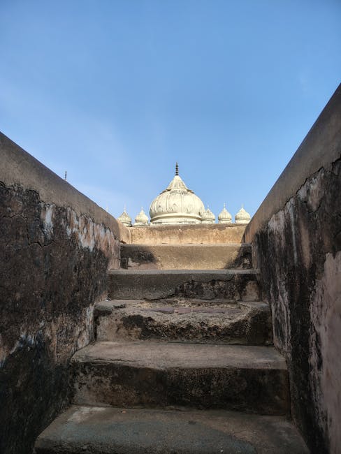 Açık mavi gökyüzünün altında tarihi bir tapınağın kubbesine çıkan yıpranmış taş basamaklar.