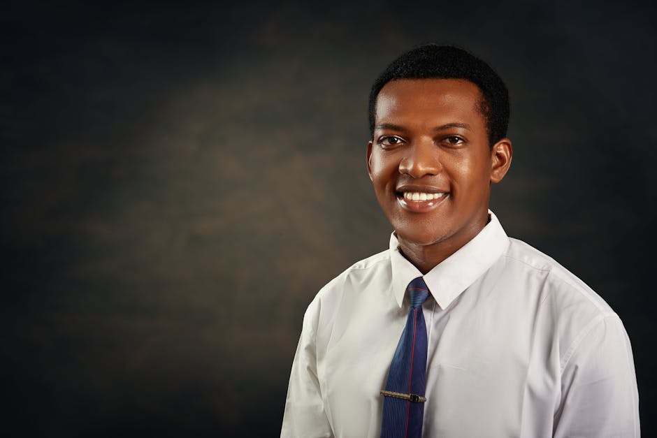 Koyu arka plan önünde resmi kıyafetli gülümseyen genç yetişkin erkek, iş veya profil kullanımı için idealdir.