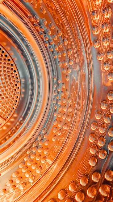 Canlı turuncu ışıklandırma ve dokularla çamaşır makinesi tamburunun dinamik yakın çekim görüntüsü.