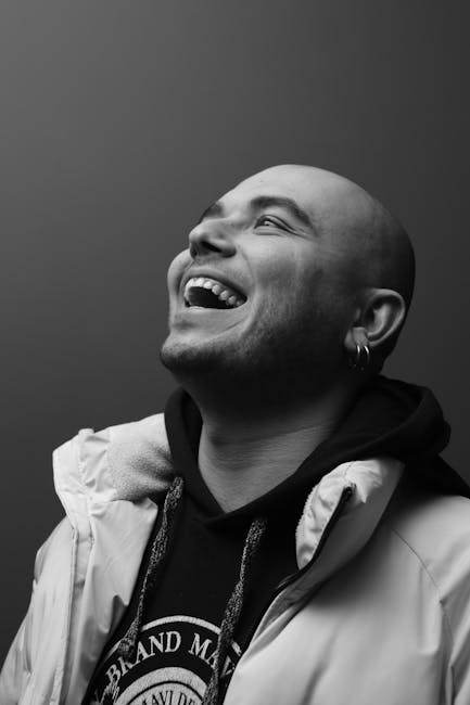 Siyah beyaz bir portrede, kel kafası tıraş edilmiş, neşeli bir adam gülüyor.