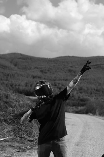 Kırsal bir yolda, doğal manzaralı bir arka plan önünde kaskıyla poz veren motosiklet sürücüsü.