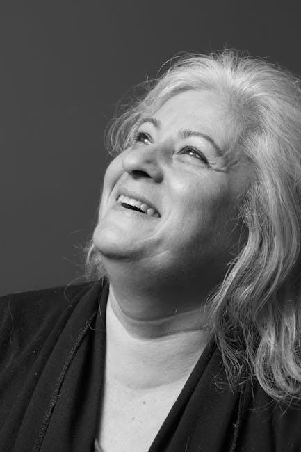 Yukarıya doğru bakan yaşlı bir kadının neşeli ifadesini yakalayan siyah beyaz portre.