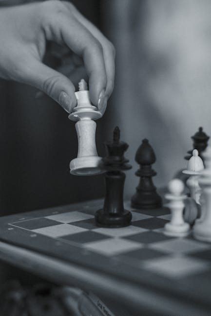 Ahşap bir satranç tahtası üzerinde insan elinin kullanıldığı stratejik bir satranç hamlesinin yakın çekimi.