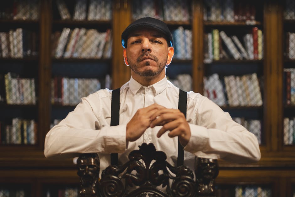 Vintage tarzda giyinmiş bir adam, kitaplarla dolu bir kütüphanede kendinden emin bir şekilde oturuyor ve klasik bir atmosfer yaratıyor.